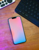 A cell phone sitting on top of a wooden table next to a keyboard
